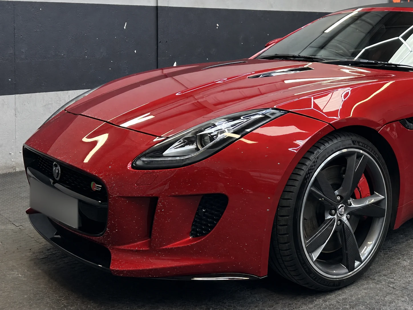 The front end of a red Jaguar F-Type with stone-chip damage across the bonnet and front wing