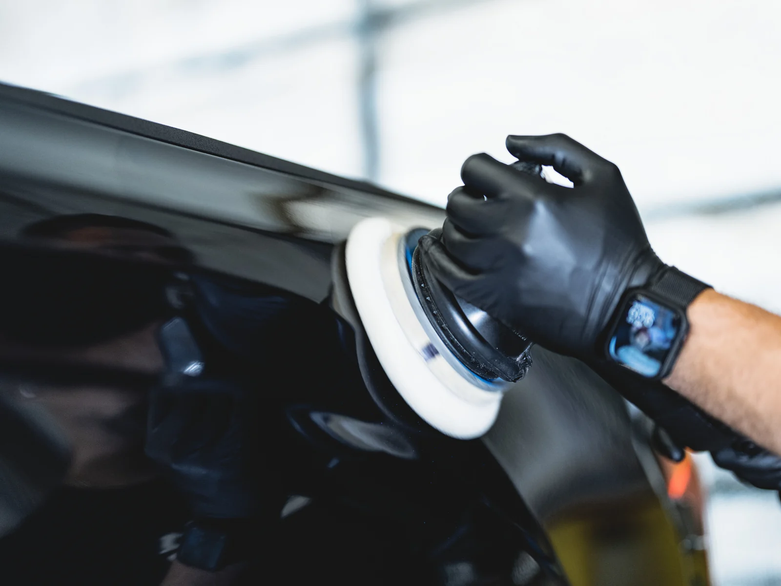 A gloved hand machine polishing a black panel with a rotary polisher