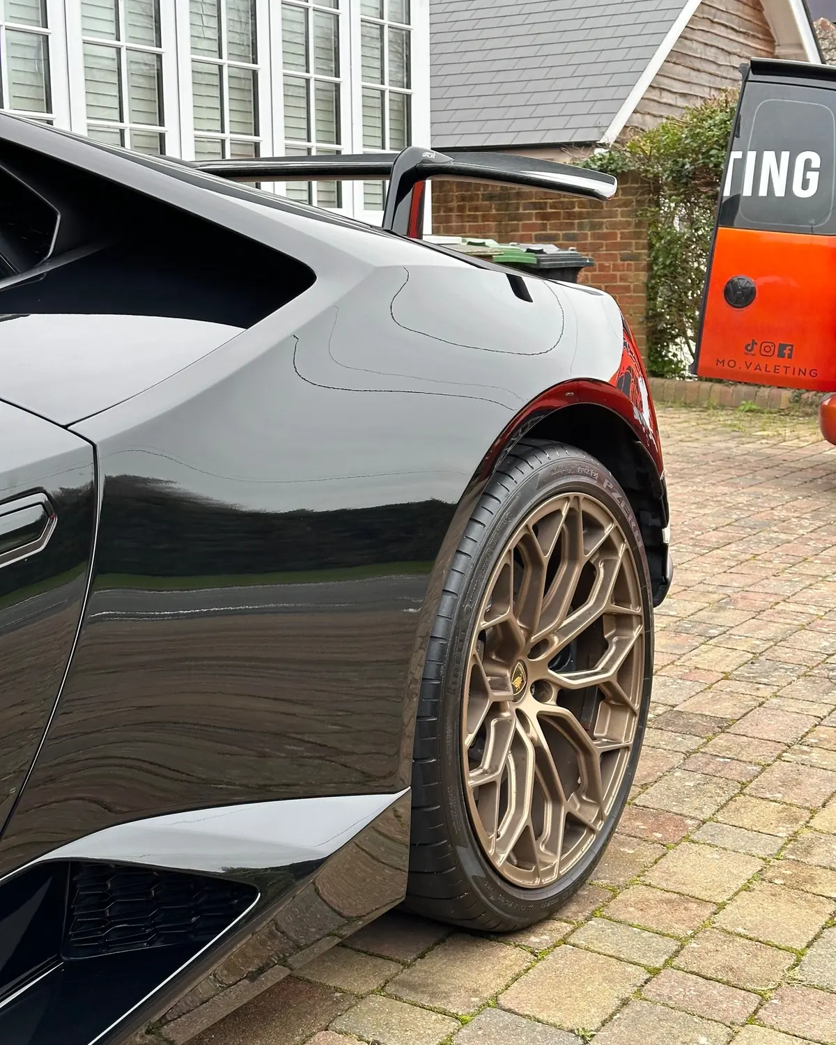 The rear quarter and wheel of a black Lamborghini Hurac&aacute;n after detailing, with the Mo&rsquo;s Valeting van behind