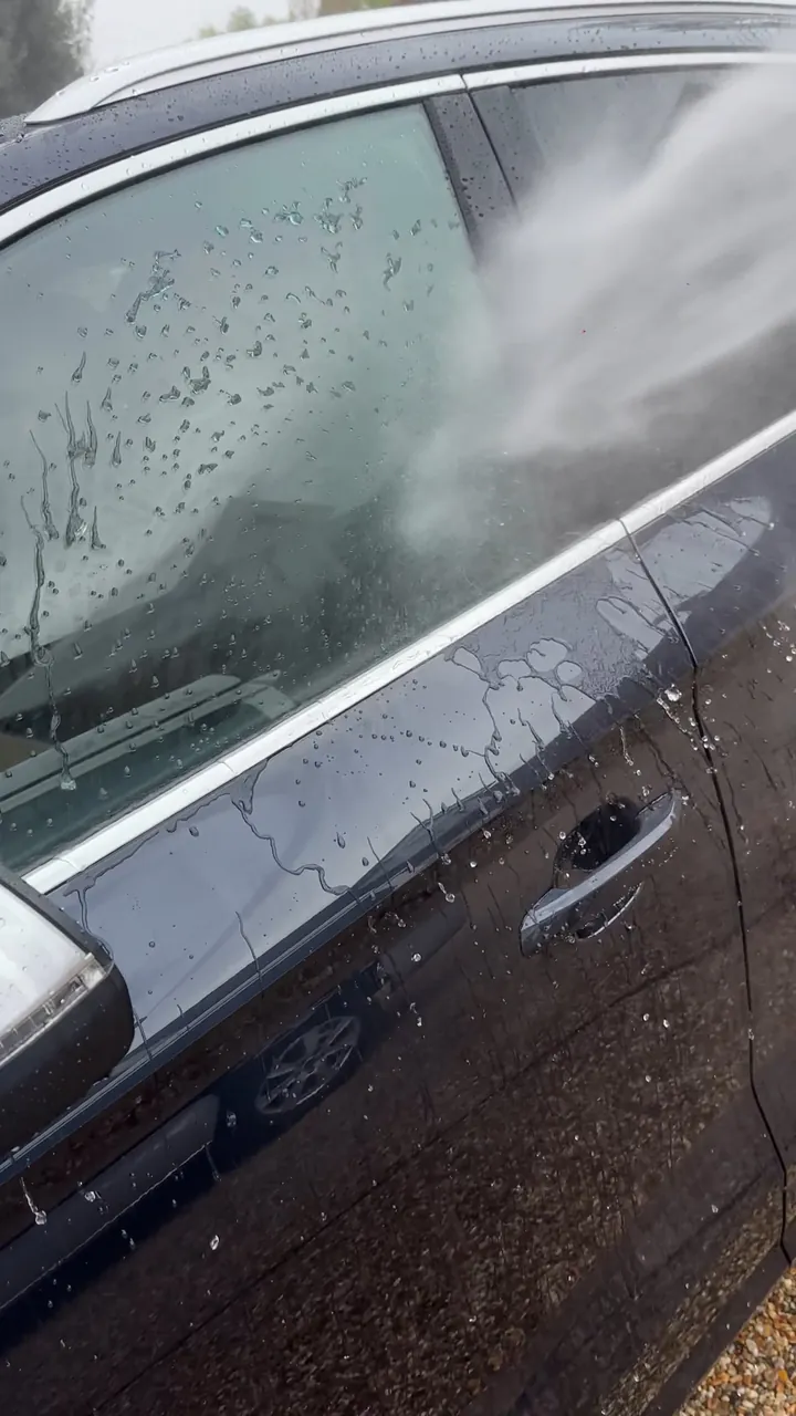 Water spraying across the door of a dark car and running off the coated paint