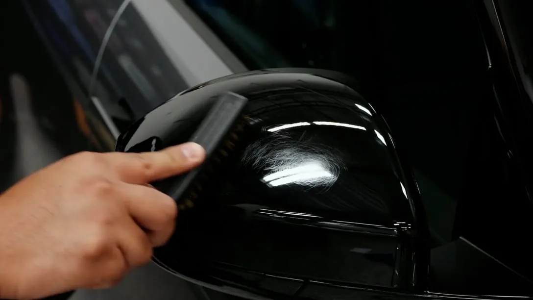 A brush being drawn across film on a gloss black wing mirror